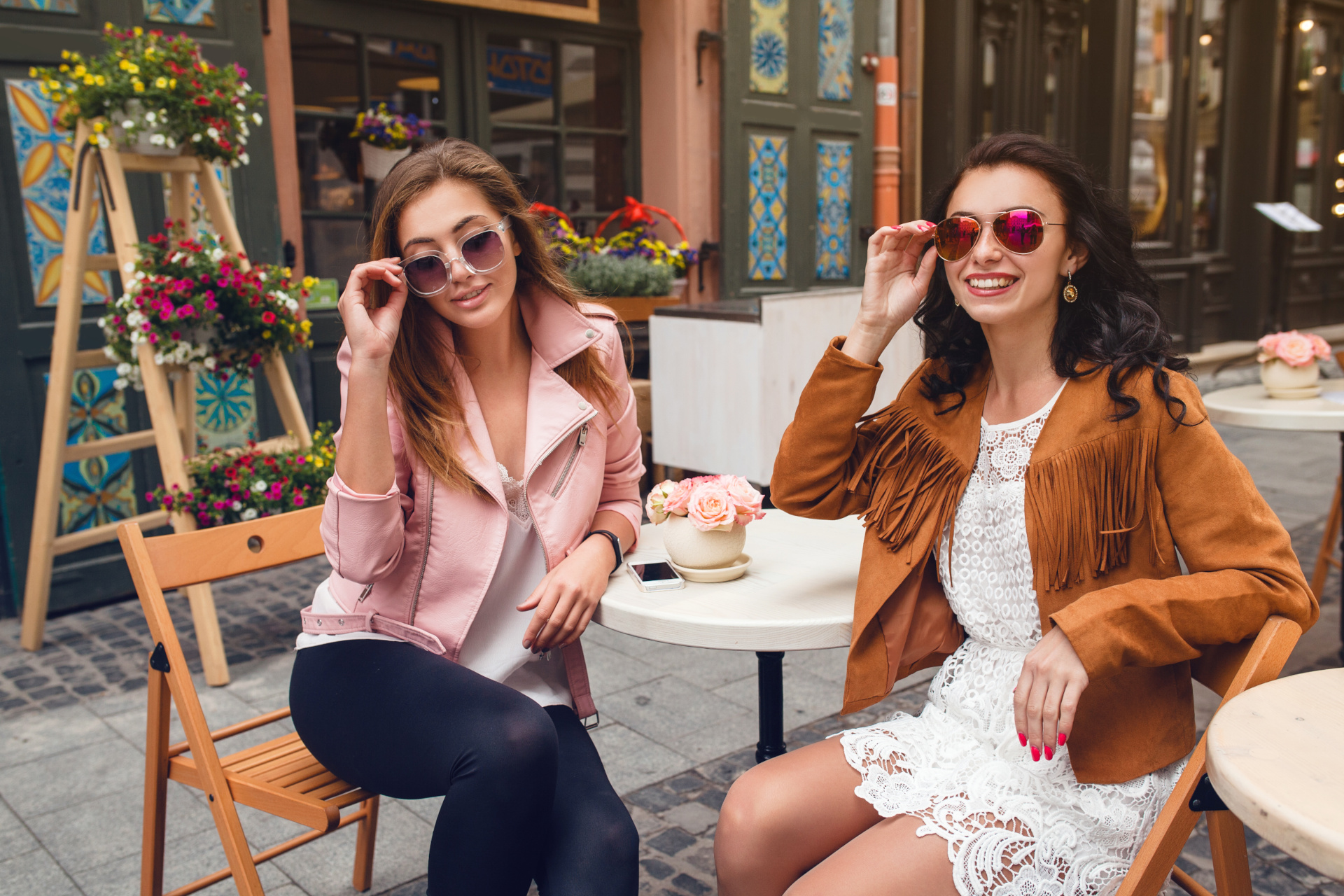 zwei junge Frauen mit Sonnenbrillen sitzen lächelnd an einem Tisch